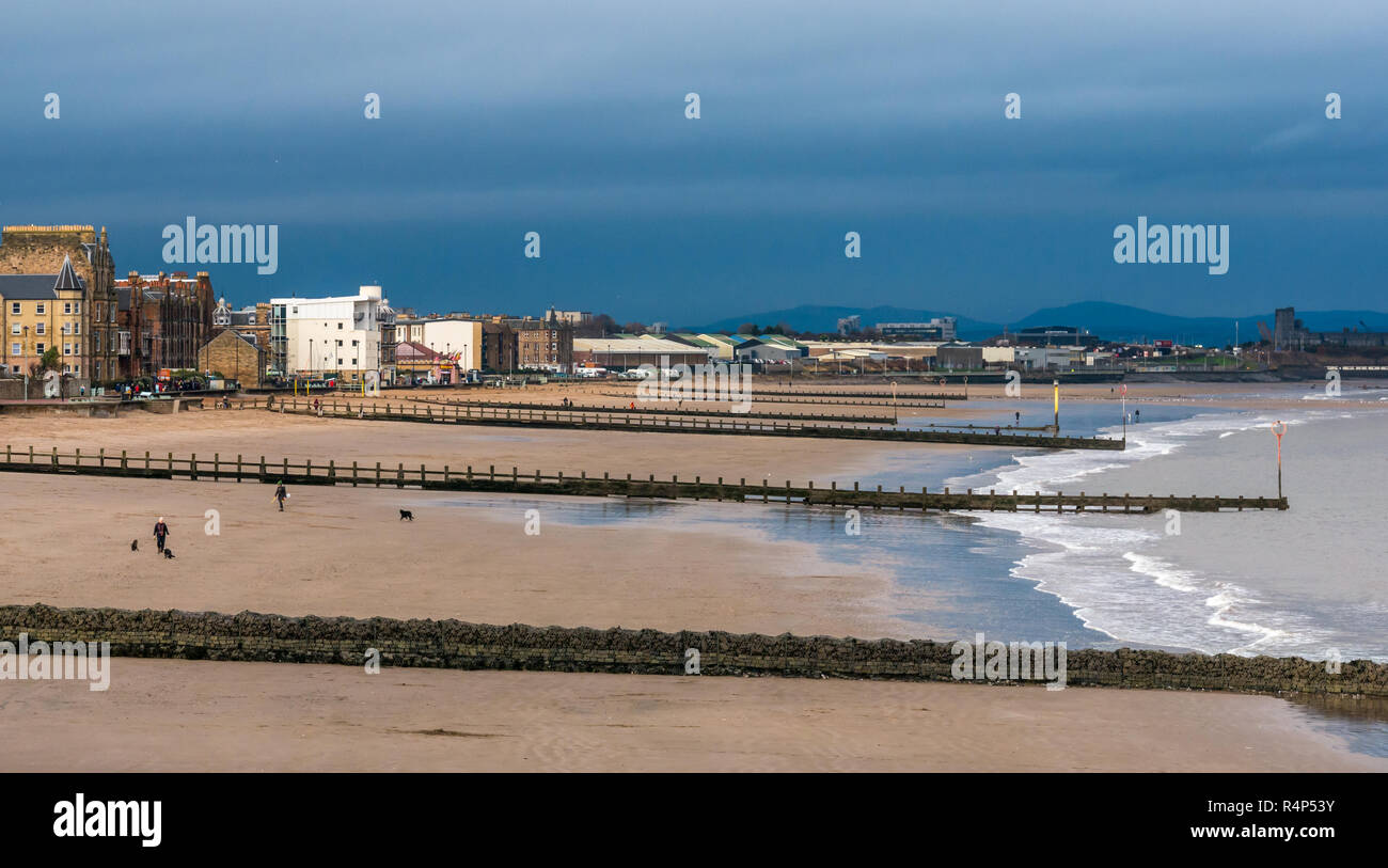 Portobello, Edinburgh, Schottland, Vereinigtes Königreich, 28. November 2018. UK Wetter: Dunkle Sturmwolken über Leute, die Hunde am Strand an der Portobello als Sturm Diana Ansätze. Der Strand verfügt über buhnen am Ufer zu schützen. Stockfoto