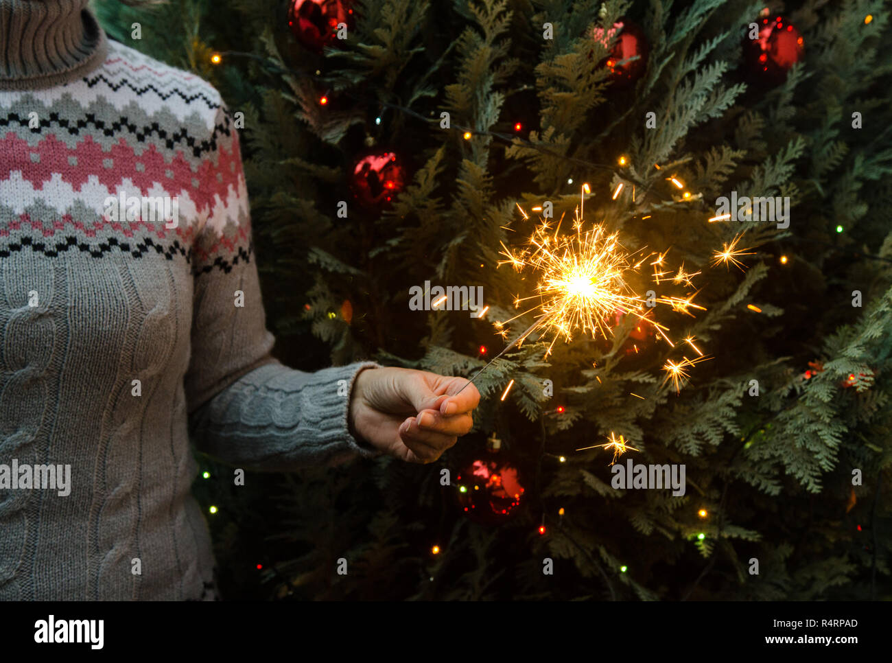Frau in Form gestrickter Pullover Wunderkerzen halten vor dem Weihnachtsbaum Stockfoto