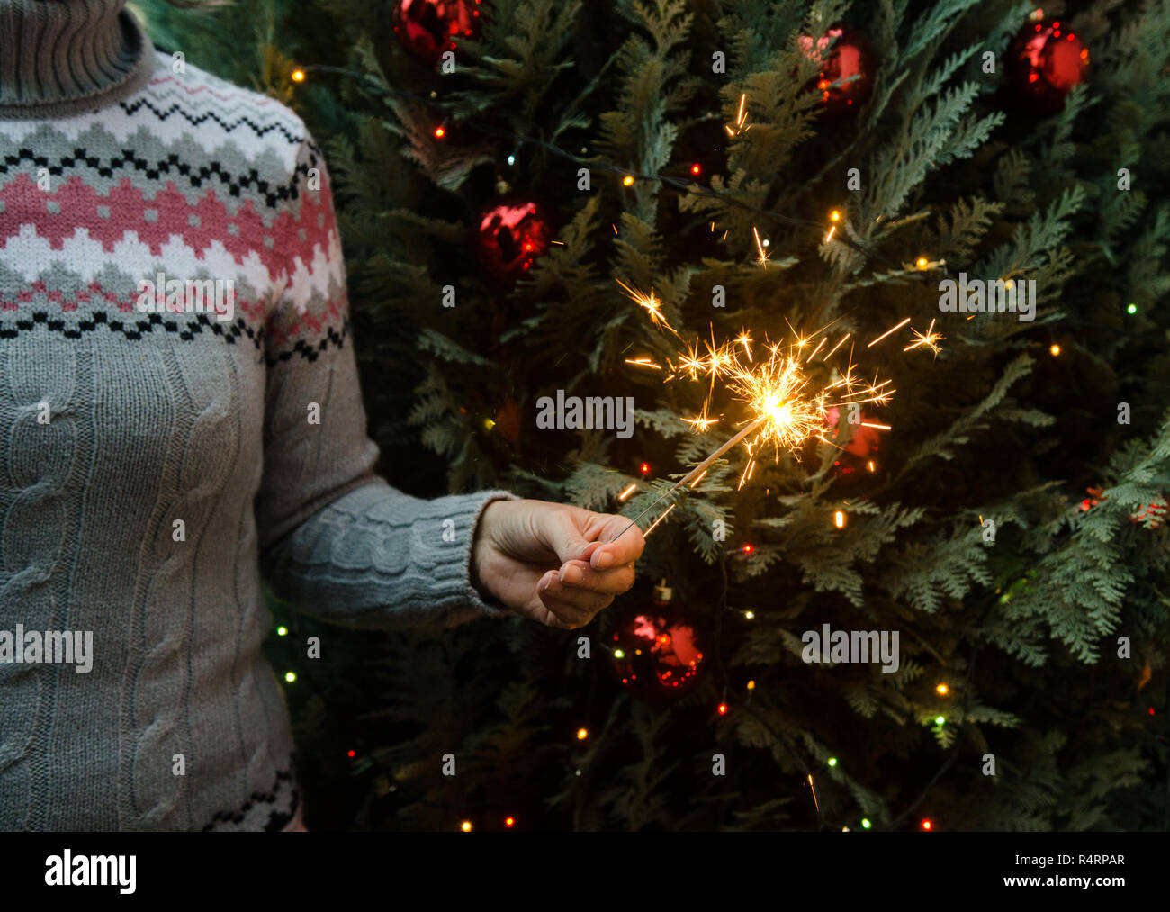 Frau in Form gestrickter Pullover Wunderkerzen halten vor dem Weihnachtsbaum Stockfoto