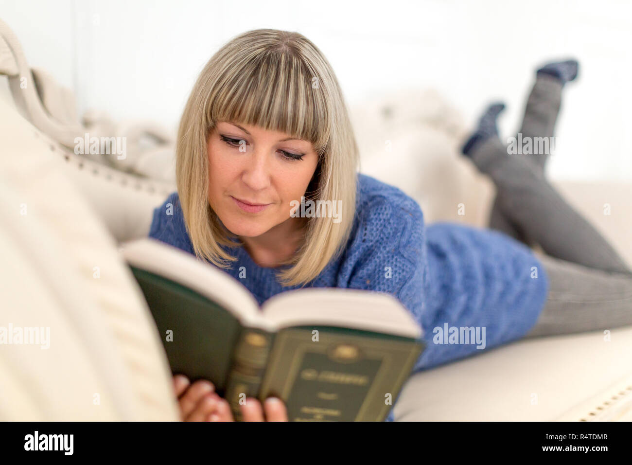 Ein Mädchen in einem blauen Kleid auf einem weißen Osmanischen ein Buch lesen Stockfoto