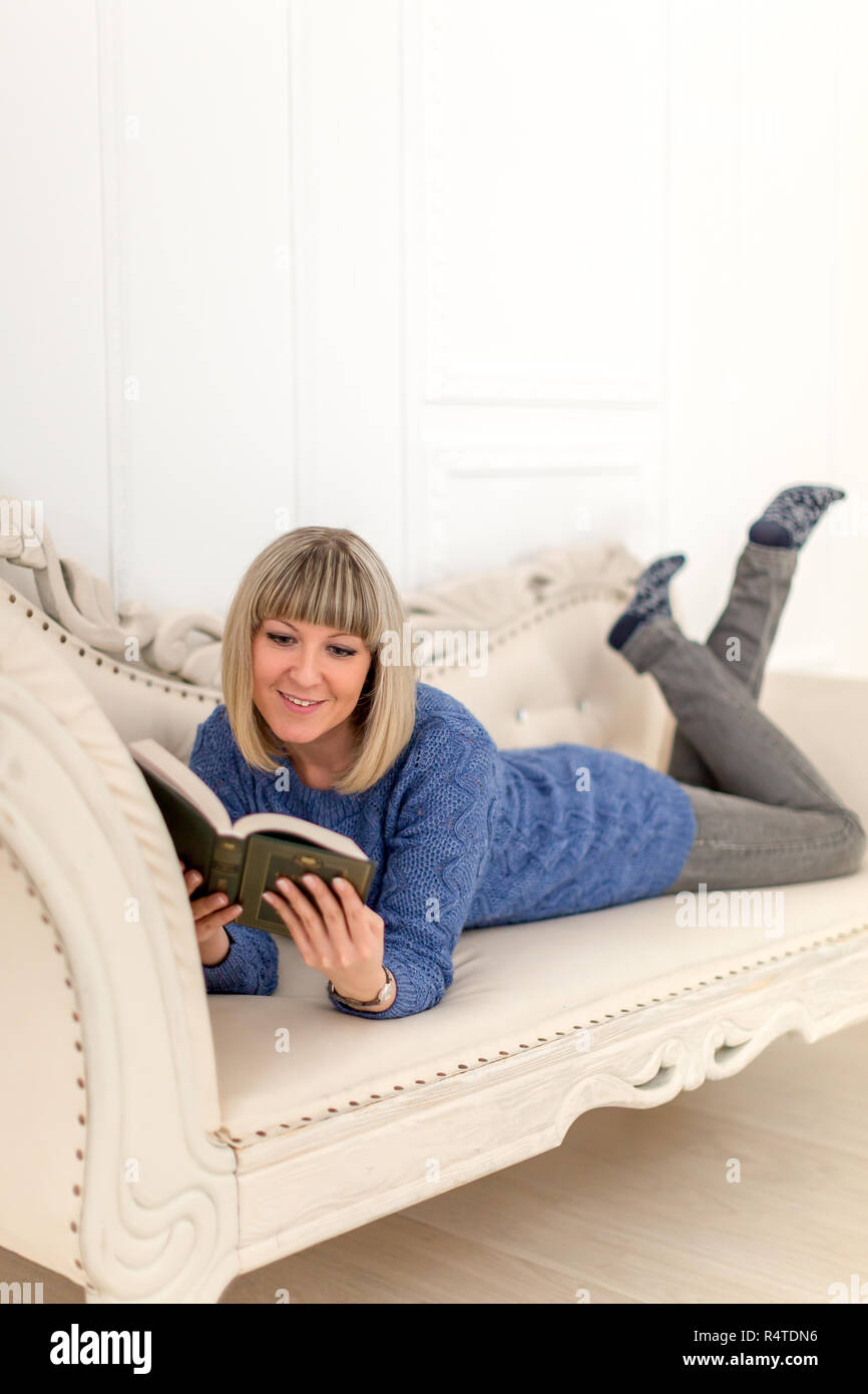Ein Mädchen in einem blauen Kleid auf einem weißen Osmanischen ein Buch lesen Stockfoto