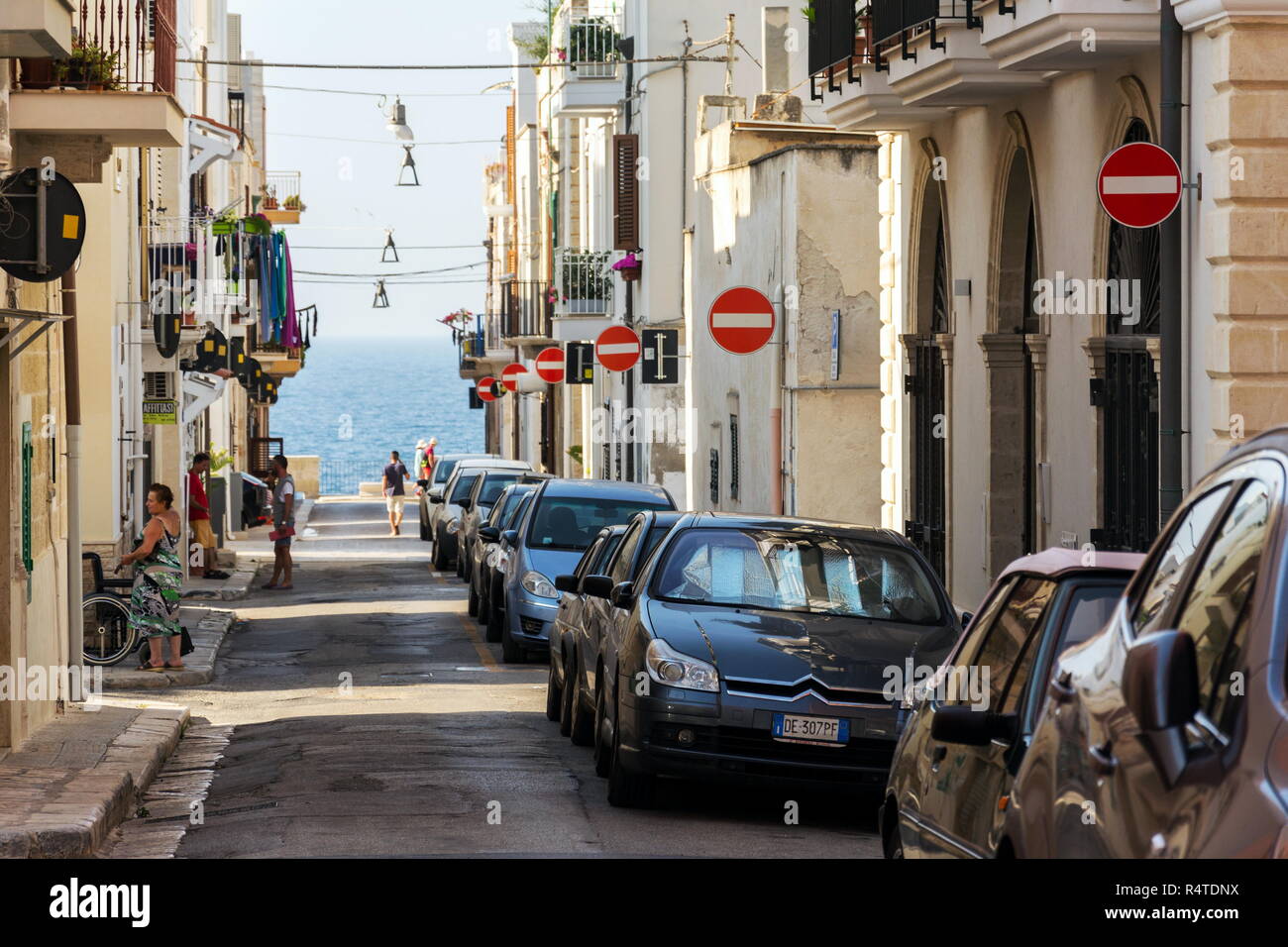 POLIGNANO A MARE, Italien - 6. JULI 2018: die Menschen entlang der parkenden Autos auf der Straße mit vielen kein Eintrag Verkehrszeichen am 6. Juli 2018 in Polignano a Mare Stockfoto