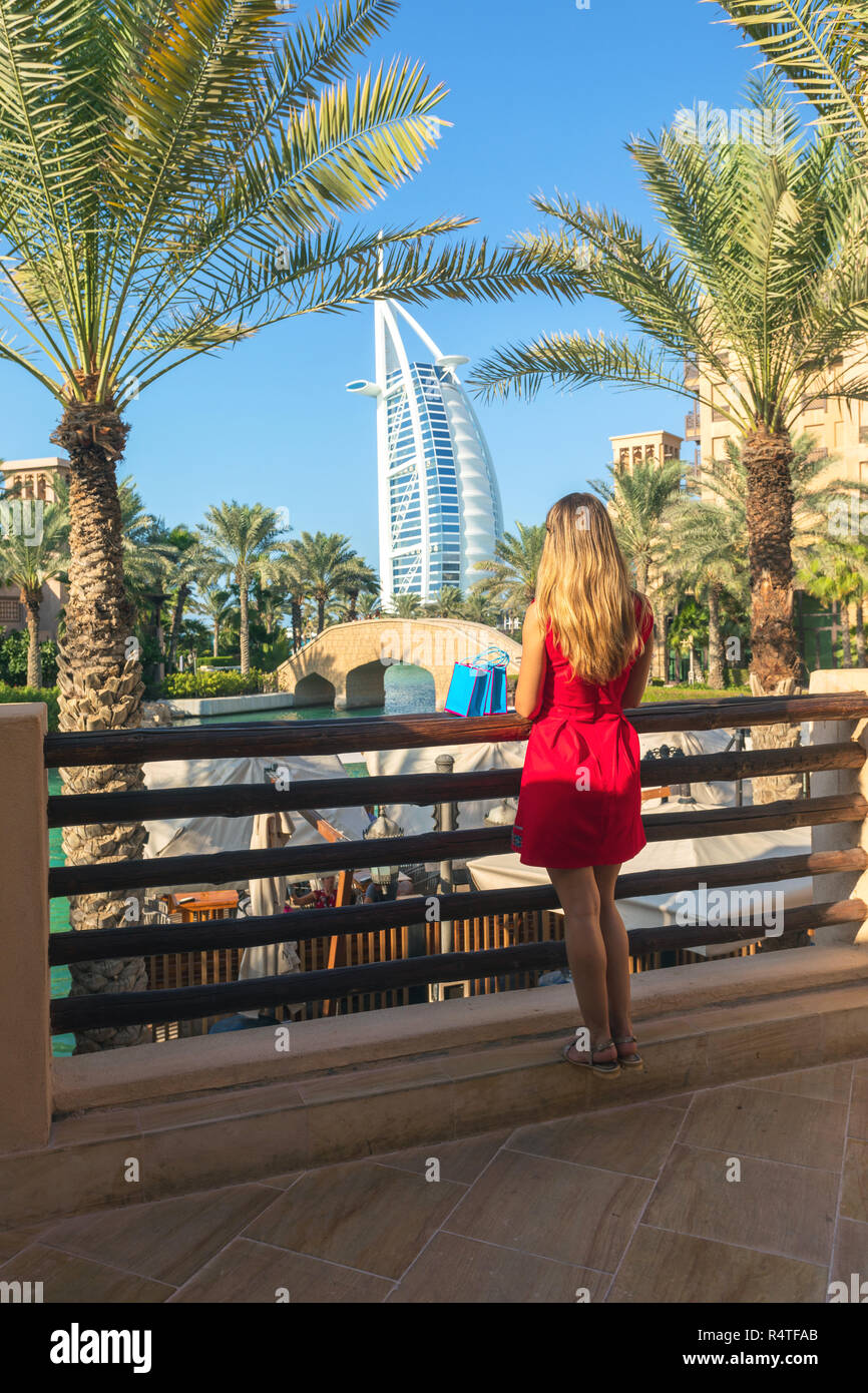 Junge touristische Frau im roten Kleid auf der Suche Burj al Arab von Madinat Jumeirah Souk mit Tüten neben ihr gekleidet. Schönes Ziel in Duba Stockfoto