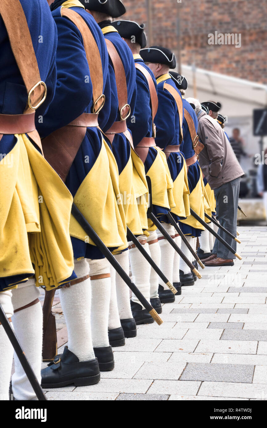 Männer in einer Reihe von schwedischen Soldaten hinter tragen historische Uniformen aus dem XVIII Jahrhundert und ein Mann ohne Kostüm, vertikal Stockfoto