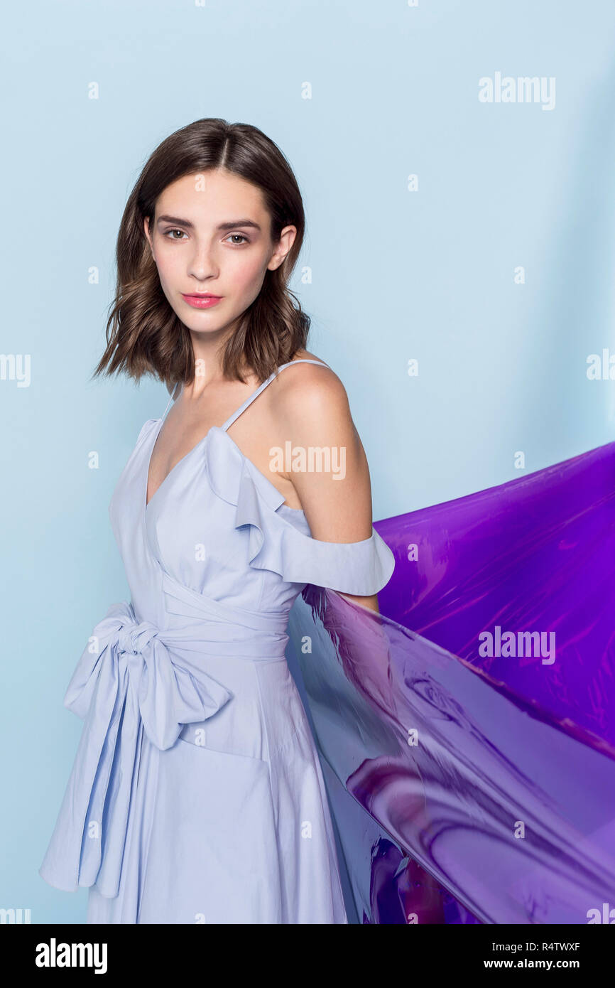 Portrait einer weiblichen Mode Modell mit lila Plastikfolie vor blauem Hintergrund posiert Stockfoto