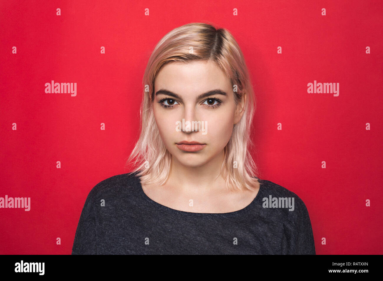 Portrait von Frau mit gebleichten Haaren und ernsten Ausdruck gegen den roten Hintergrund Stockfoto