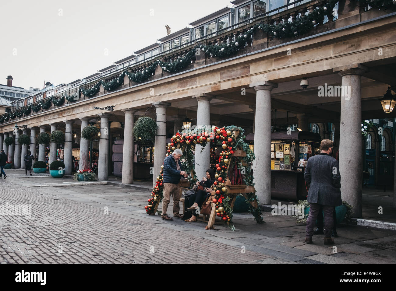 London, UK, November 21, 2018: Menschen bei einer Bank mit Christbaumkugeln in Covent Garden Market, einem berühmten touristischen Bereich in London wi eingerichtet sitzen Stockfoto
