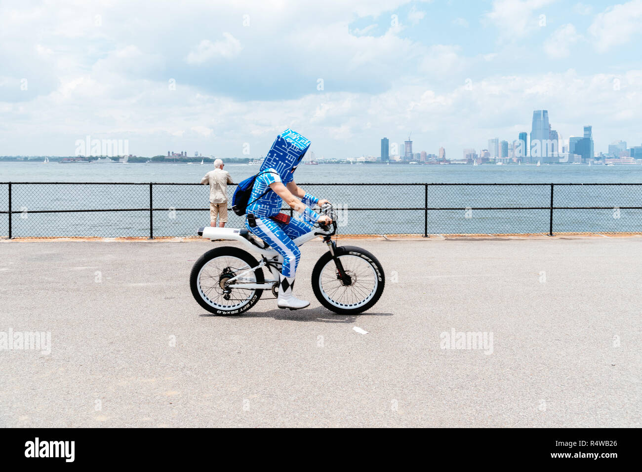 New York City, USA - 24. Juni 2018: Der Mann mit dem Fahrrad entlang der Promenade in Governors Island trägt einen Karton auf dem Kopf gegen Skyline Stockfoto