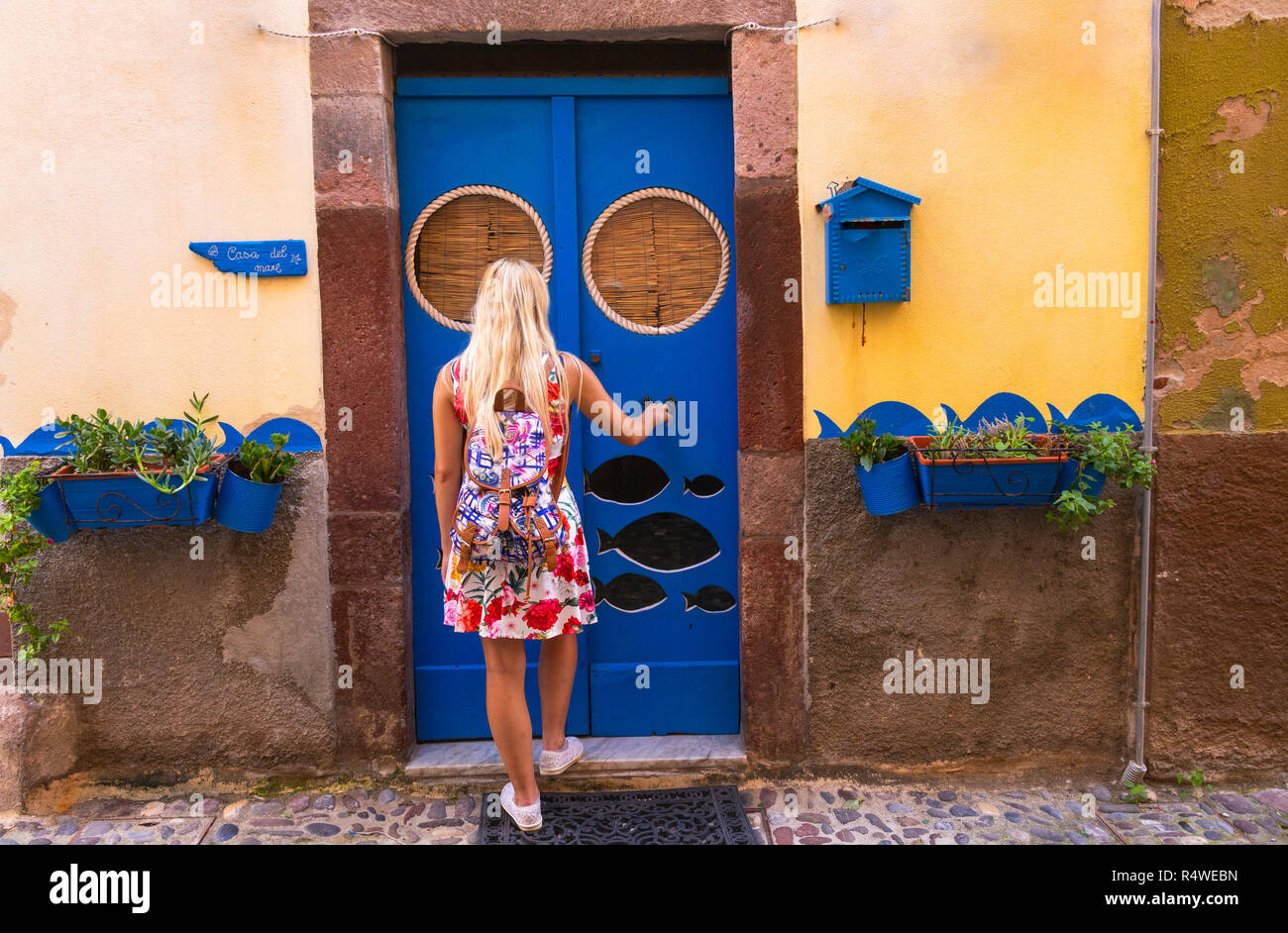 Mädchen klopft auf einer blauen Tür. Bosa, Provinz Oristano, Sardinien, Italien, Europa. Stockfoto