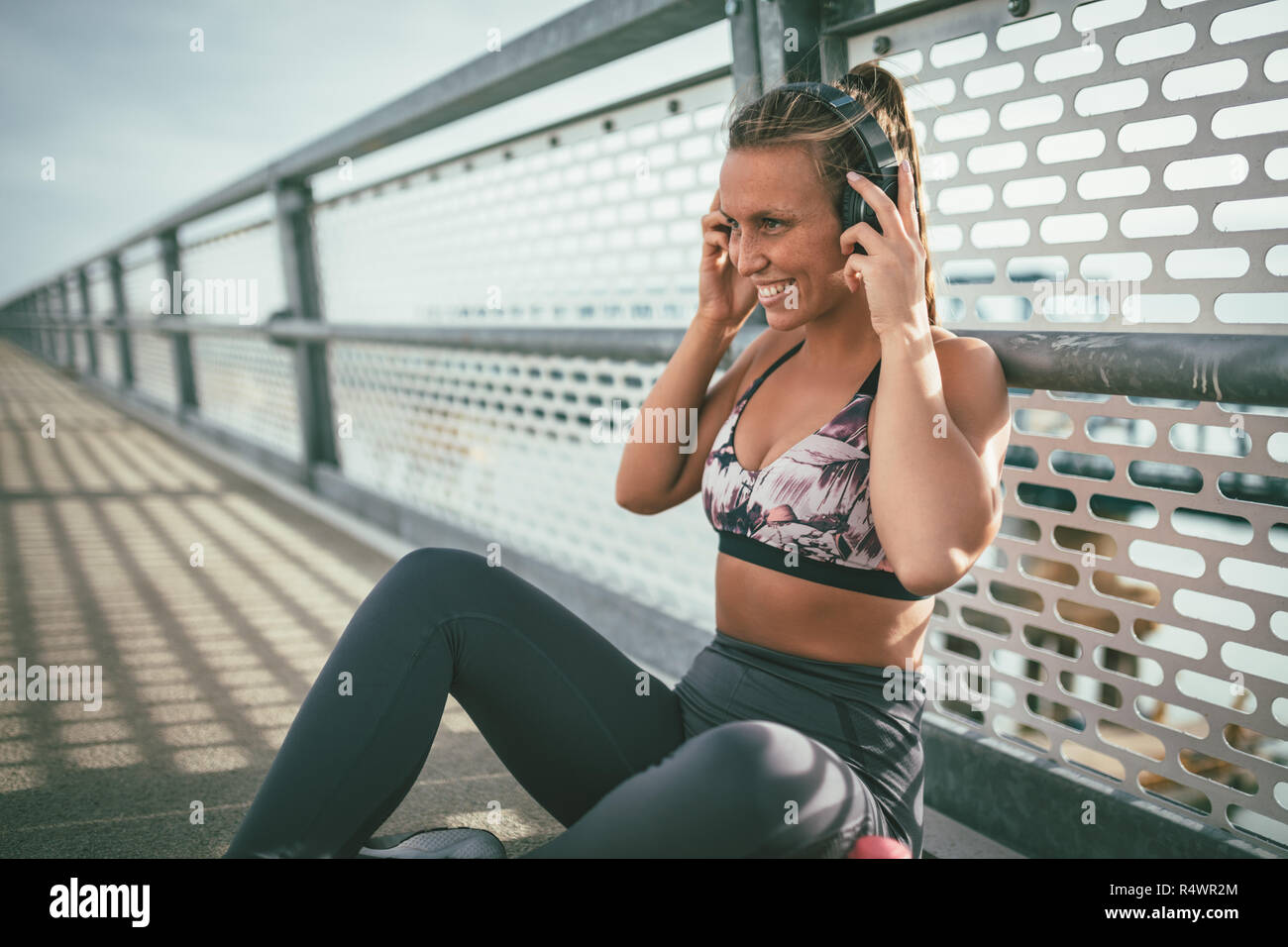 Junge fitness Frau ruht sich nach harten Training auf der Brücke über den Fluss und setzen Ihre Ohrhörer. Stockfoto