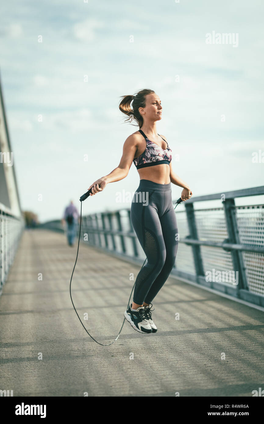 Junge Läuferin über Springseil und Übung auf einer Brücke über den Fluss springen, Vorbereitung für Morgen Workout. Stockfoto