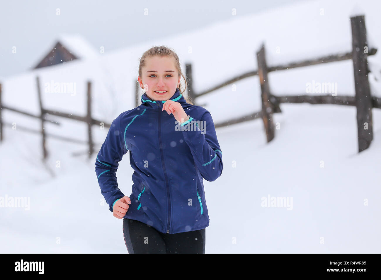 Junges Mädchen läuft auf Winter Mountain Trail. Lächelnde Mädchen beim Joggen in der kalten verschneiten Morgen Stockfoto