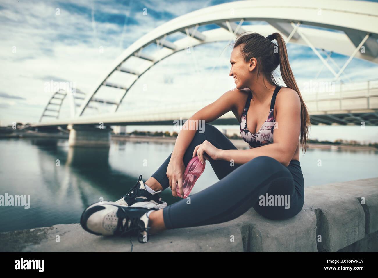 Junge fitness Frau ruht sich nach harten training durch die Brücke über den Fluss Trinkwasser. Stockfoto