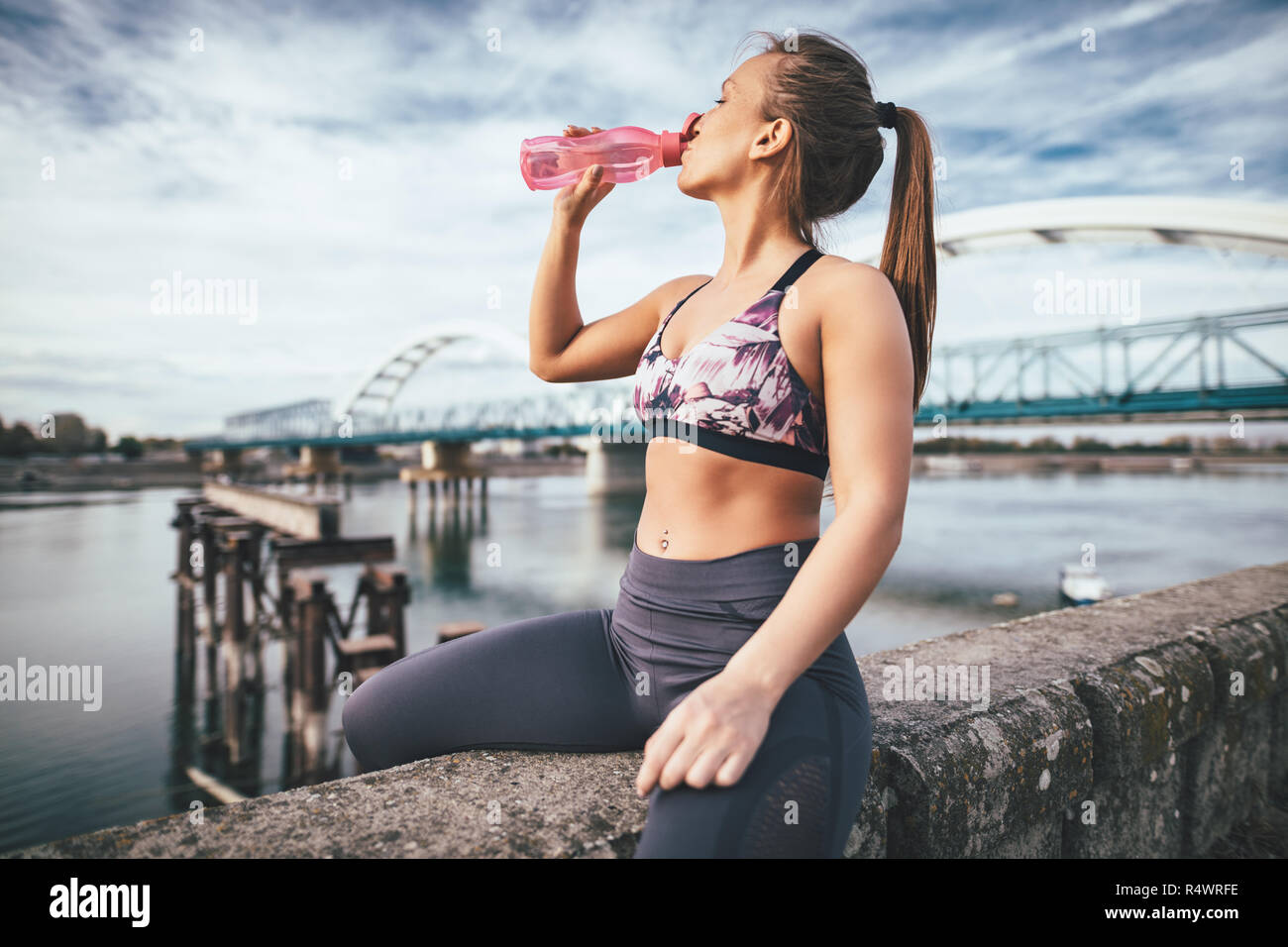 Junge fitness Frau ruht sich nach hartem Training an der Wand von der Brücke über den Fluss und Trinkwasser. Stockfoto