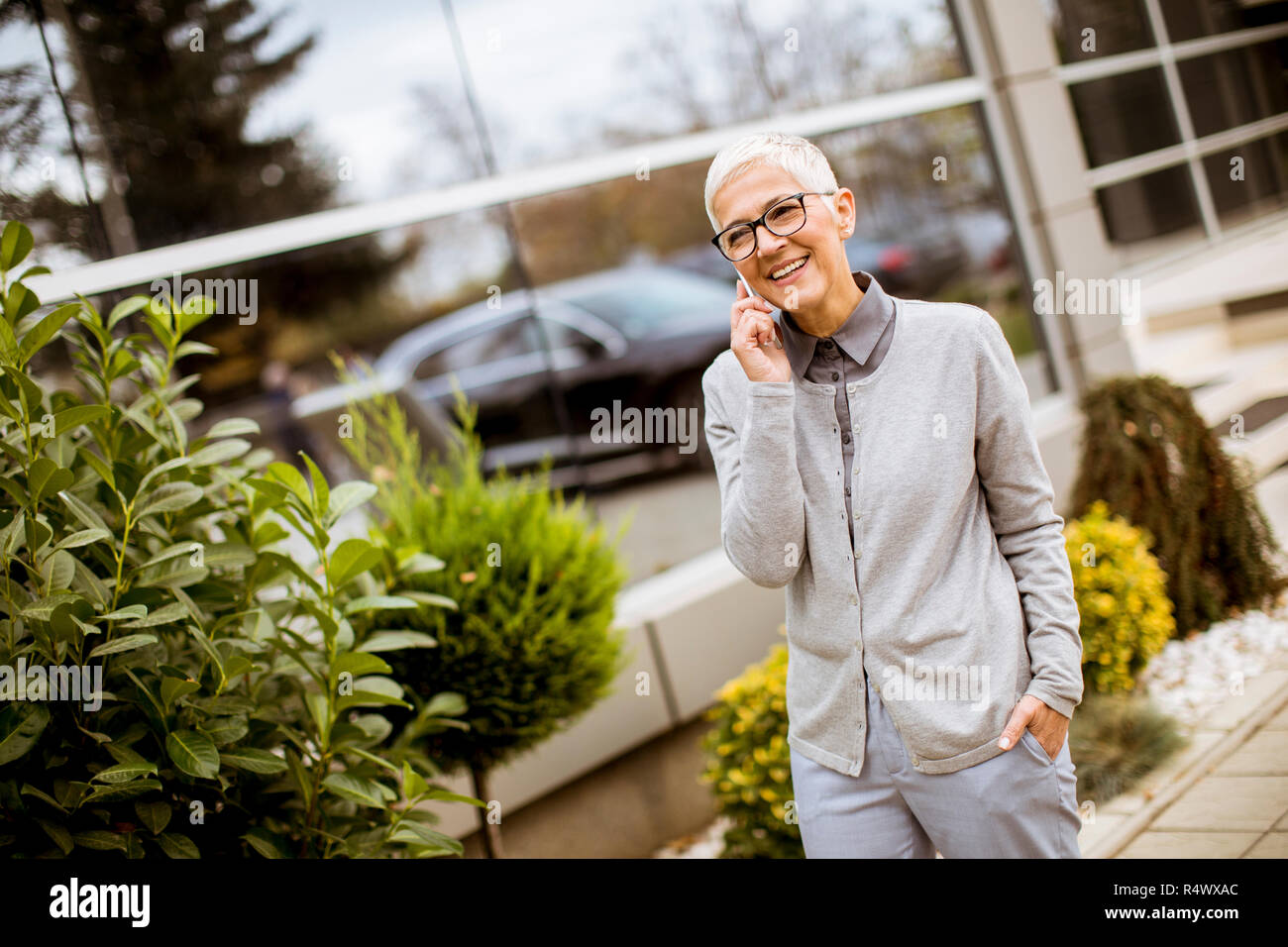 Lächelnd senior Geschäftsfrau, am Telefon zu sprechen, während sie vor einem Bürogebäude steht. Stockfoto