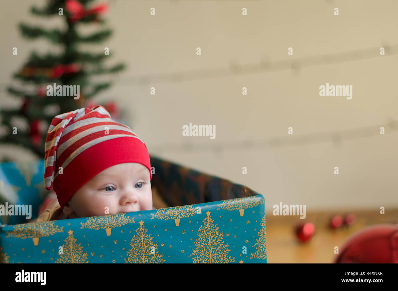 Happy Christmas baby boy in einem derzeitigen Kasten um Weihnachtsbaum und Dekorationen Stockfoto