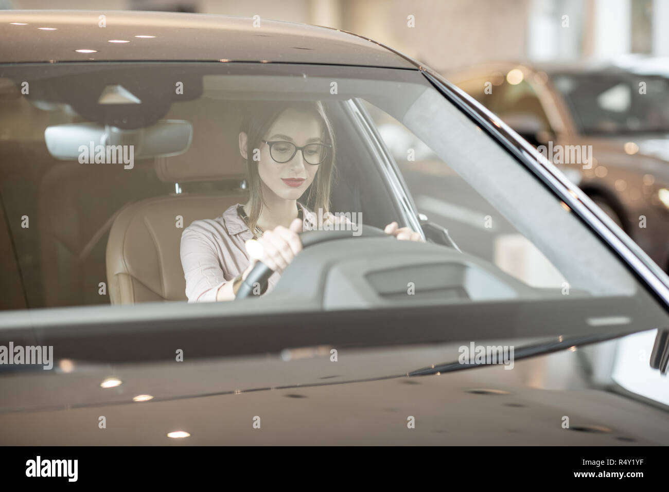 Junge Frau bei der Auswahl eines neuen Auto sitzen auf dem Fahrersitz eines Luxuswagens im Showroom Stockfoto