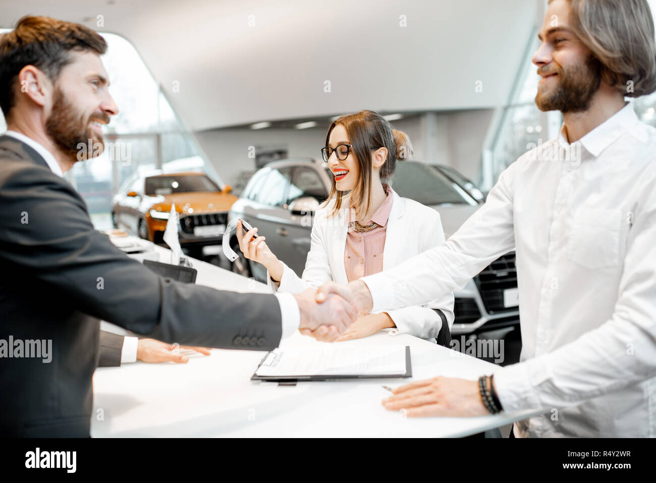 Young Business Paar Hände schütteln in einen Deal mit Verkäufer am Stand den Kauf oder die Vermietung von Auto im Showroom Stockfoto