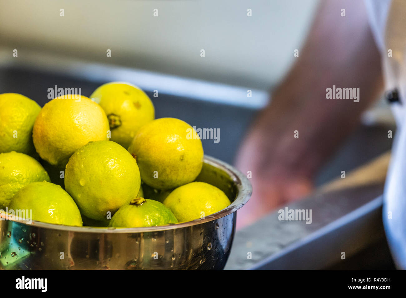 Frisch gewaschene Limetten in der Schüssel - Verschwommenes Chef's Hände im Hintergrund Stockfoto