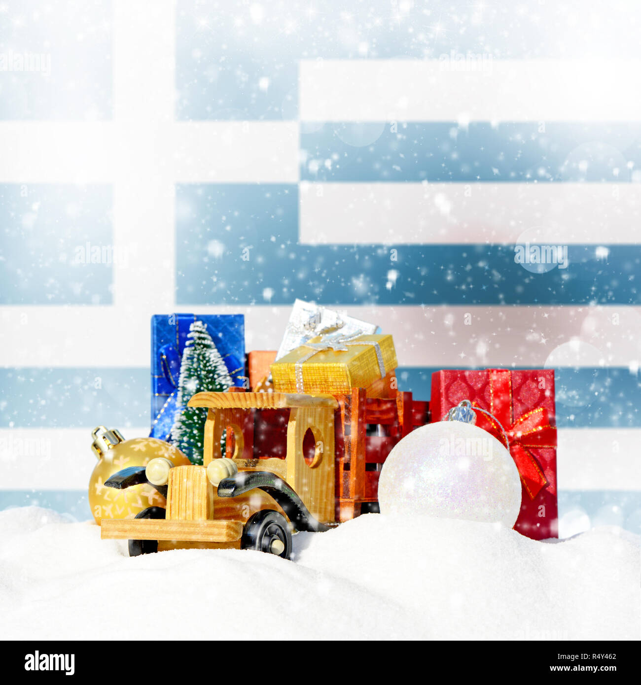Weihnachten Hintergrund. Spielzeug-LKW mit Geschenken, Neues Jahr Tanne, Kugeln im Schneetreiben und griechische Flagge Stockfoto