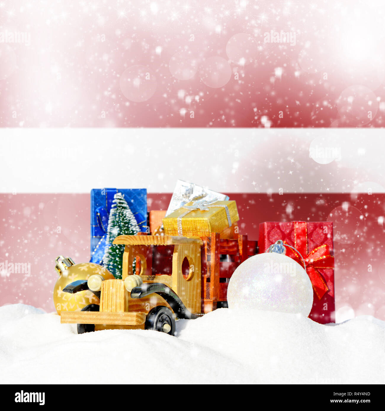 Weihnachten Hintergrund. Spielzeug-LKW mit Geschenken, Neues Jahr Tanne, Kugeln im Schneetreiben und lettischer Flagge Stockfoto
