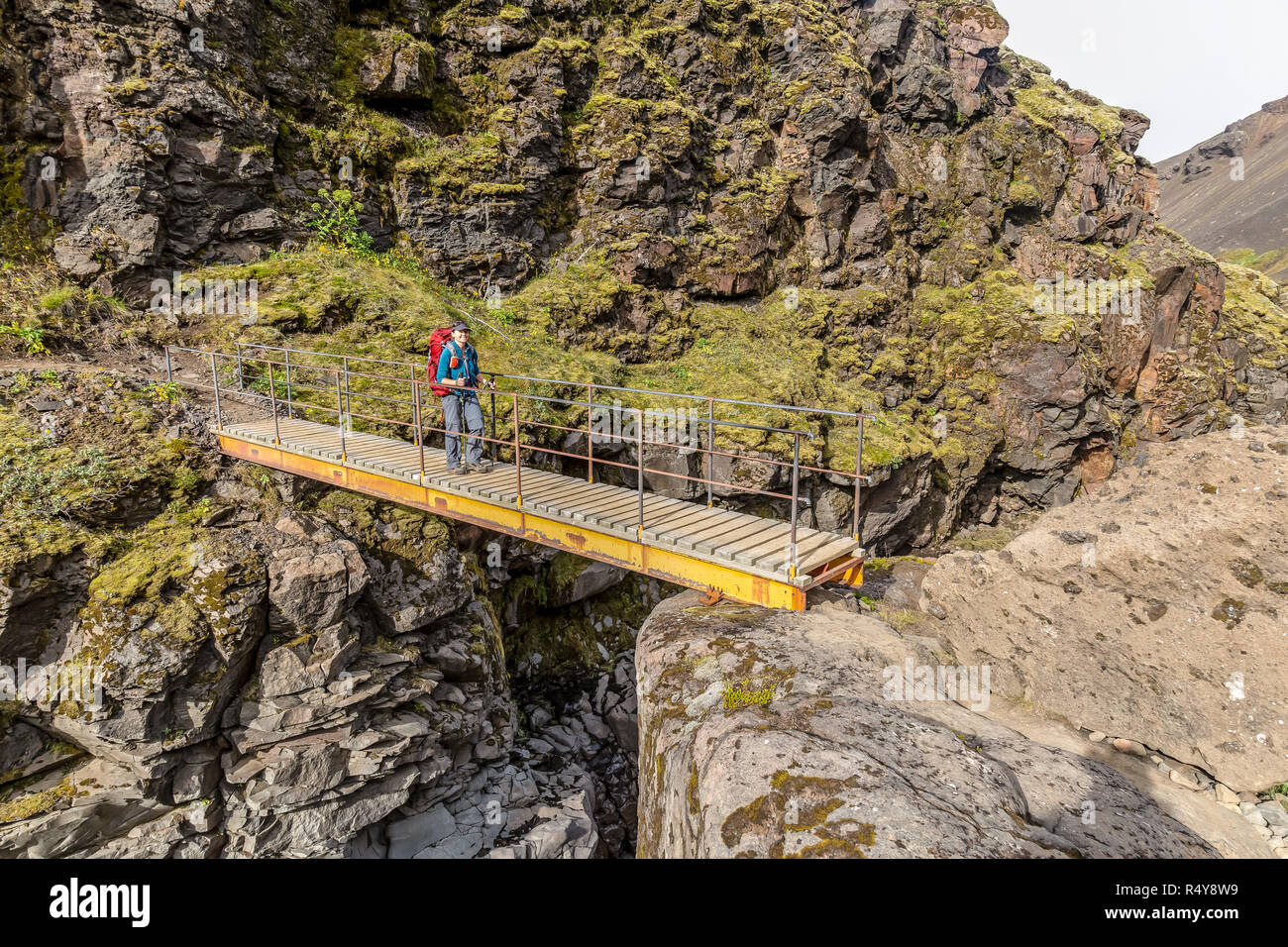 Eine einsame weibliche Wanderer über eine Brücke über einen Fluss Schlucht auf der Laugavegur Trail in Island. Stockfoto