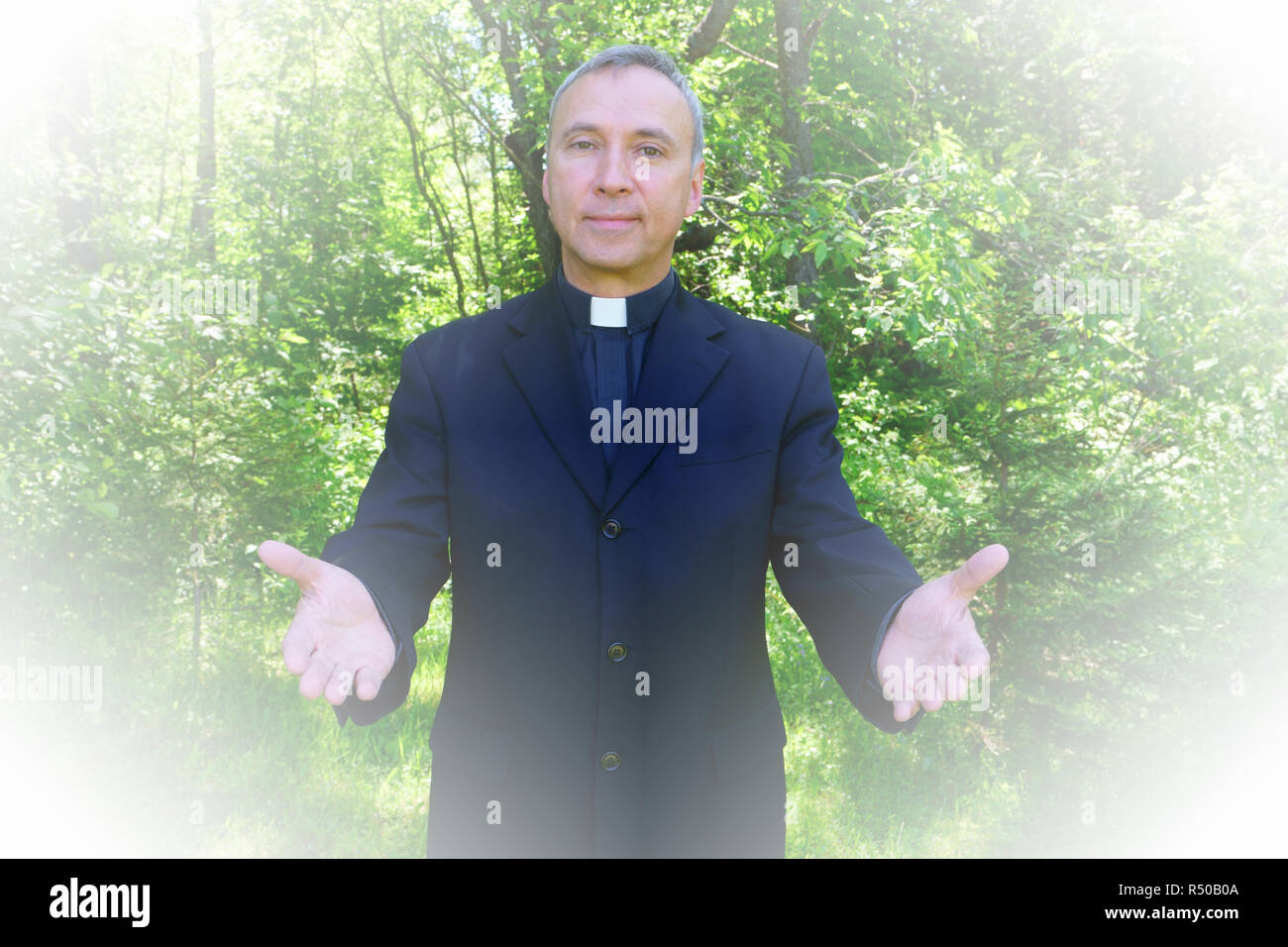 Ein katholischer Priester uns ist einladend in der Freude. Er schaut mit Vertrauen an uns, seine Arme öffnen in Frieden. Stockfoto