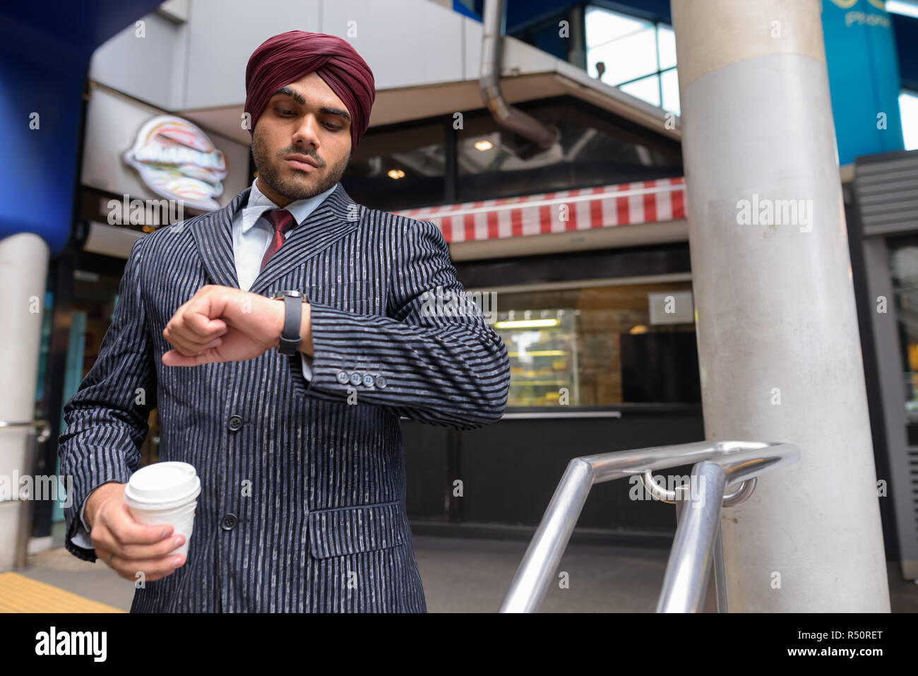 Indische Sikh Geschäftsmann Kontrolle smart Watch und halten Kaffee Stockfoto