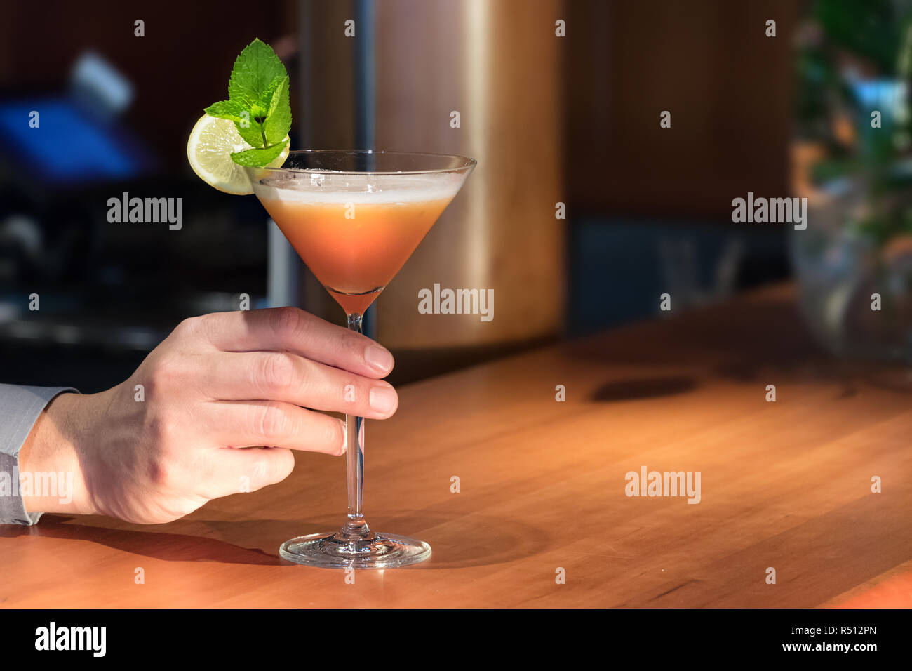 Ein Barkeeper Hand einen Martini trinken ein Glas auf einer hölzernen Zähler dienen. Stockfoto