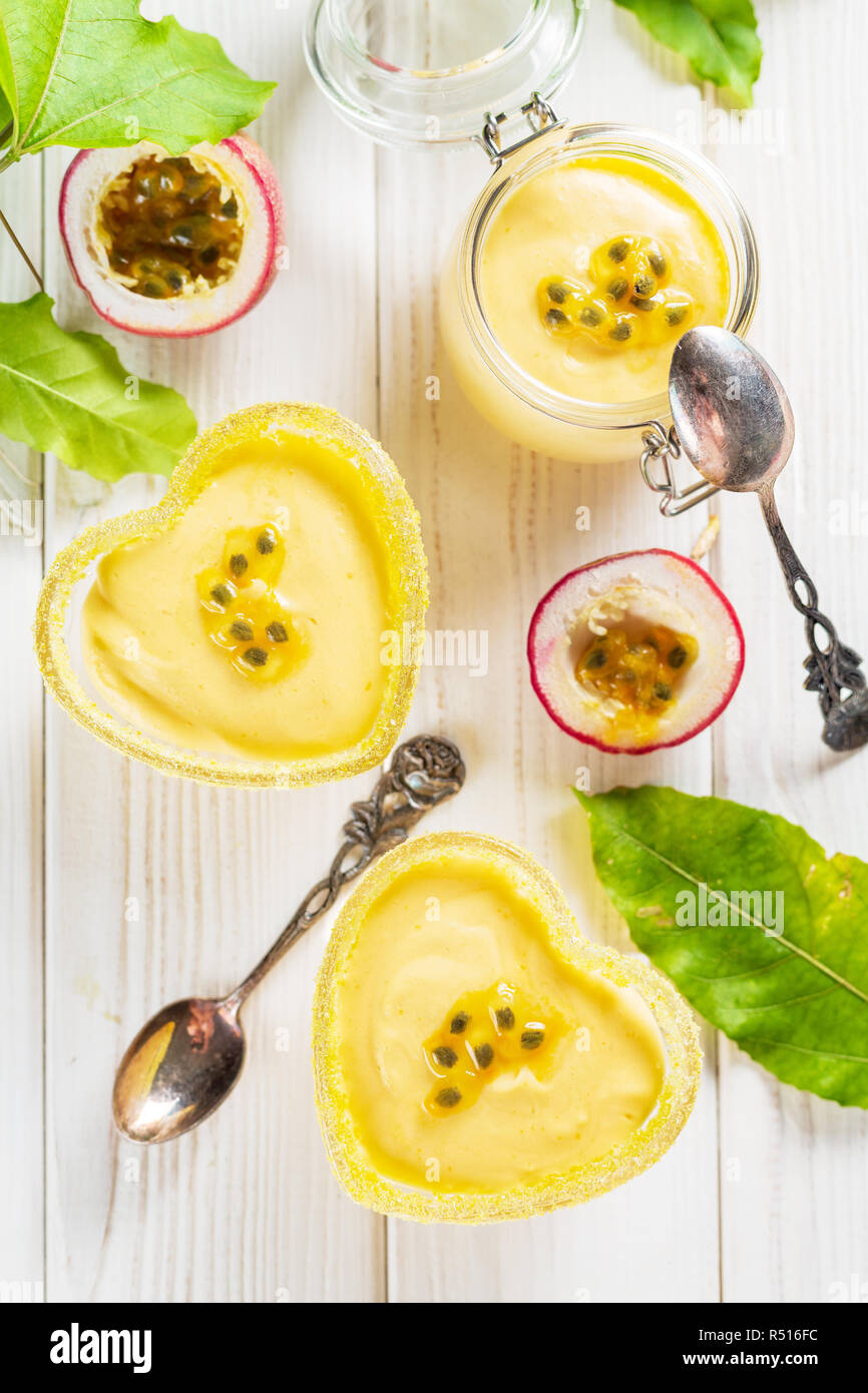 Glas Glas und zwei Herzen Glas Förmchen mit Passionsfrucht Mousse auf weißem Hintergrund, vertikale Komposition aus Holz Stockfoto