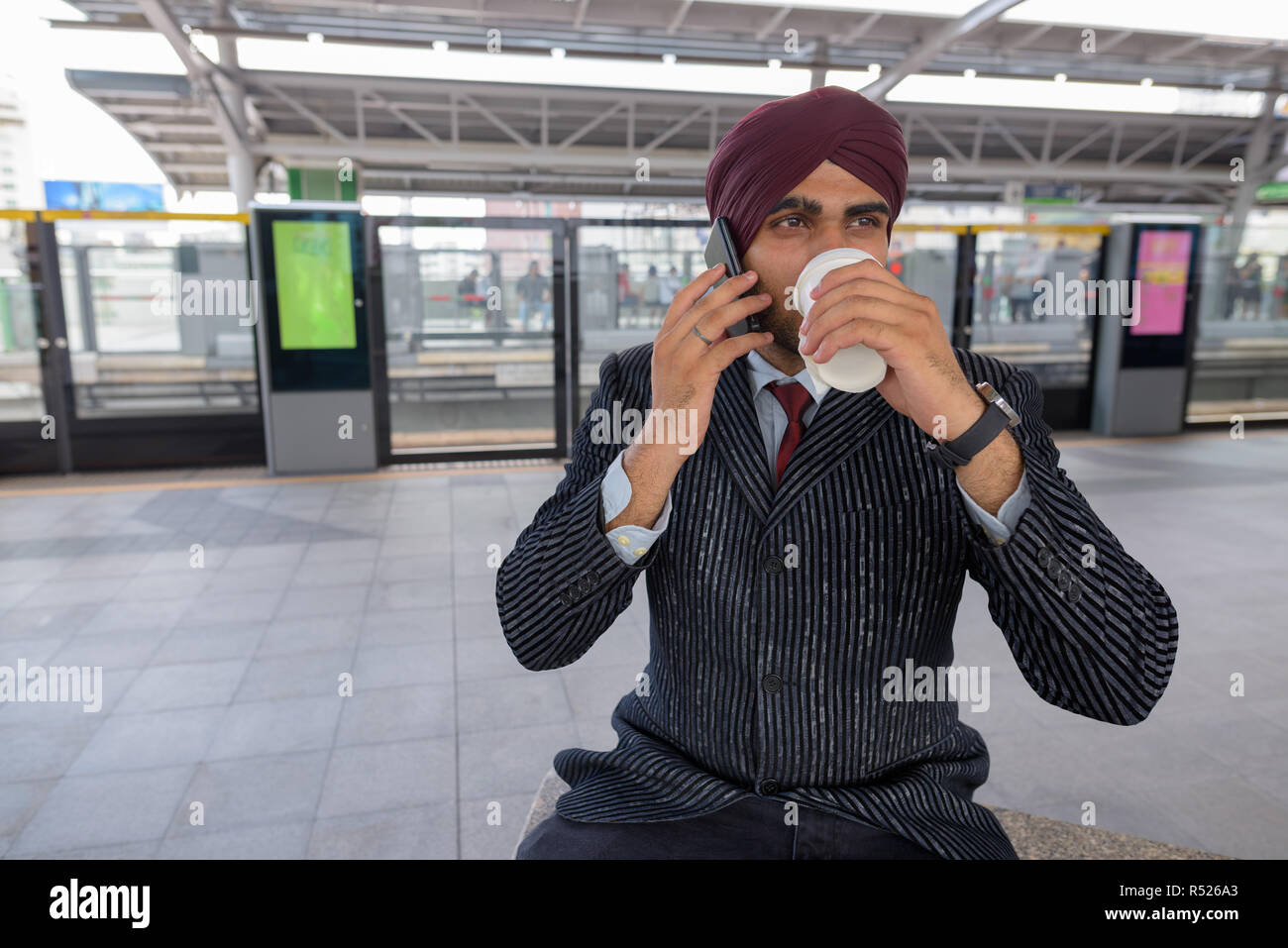 Indischer Geschäftsmann am Telefon sprechen am Bahnhof beim Trinken von Kaffee Stockfoto