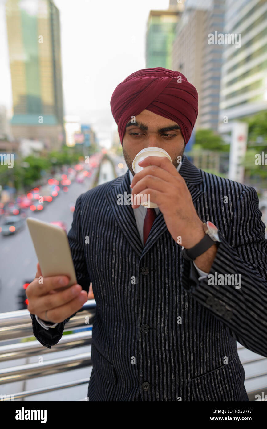 Indischer Geschäftsmann im Freien in der Stadt mit Handy und trinken Kaffee Stockfoto