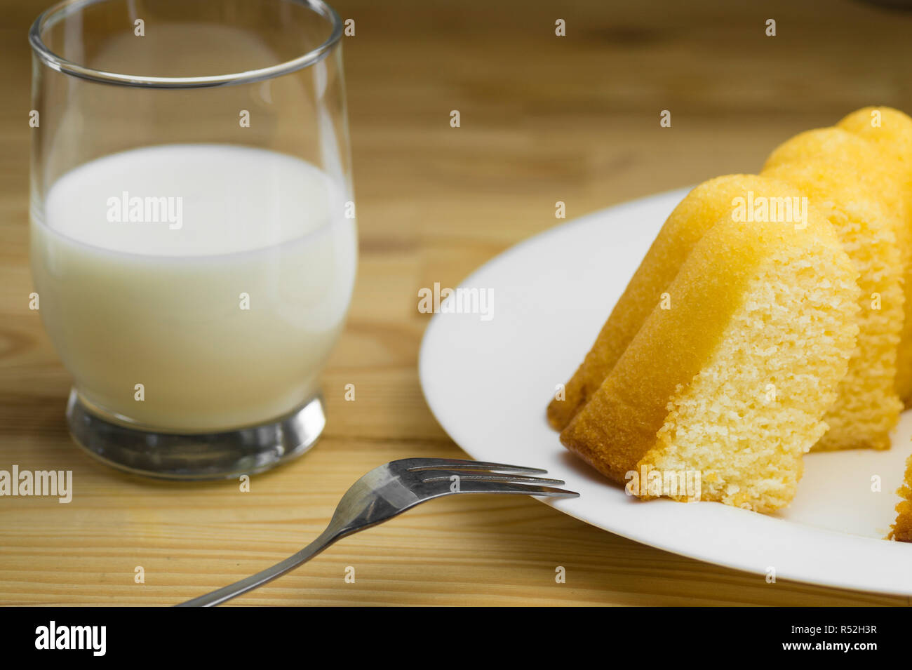 Nahaufnahme der hausgemachten Zitronenkuchen auf einem weißen Teller und ein Glas frische Milch auf einen hölzernen Tisch. Stockfoto