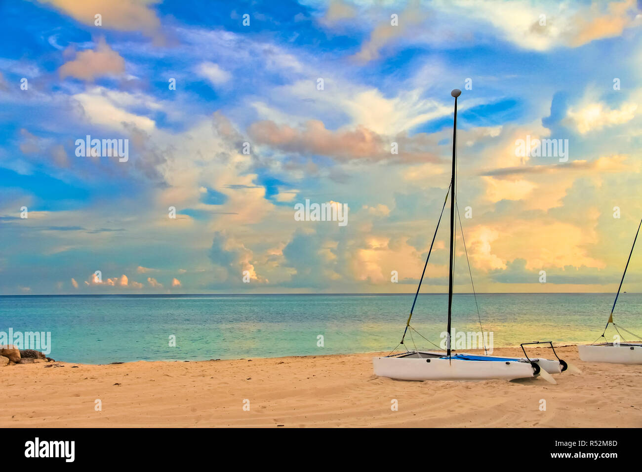 Katamaran an einem tropischen Strand durch das türkisfarbene Wasser der Karibik, Freeport, Bahamas und atemberaubenden Wolken im Hintergrund bei Sonnenuntergang Stockfoto