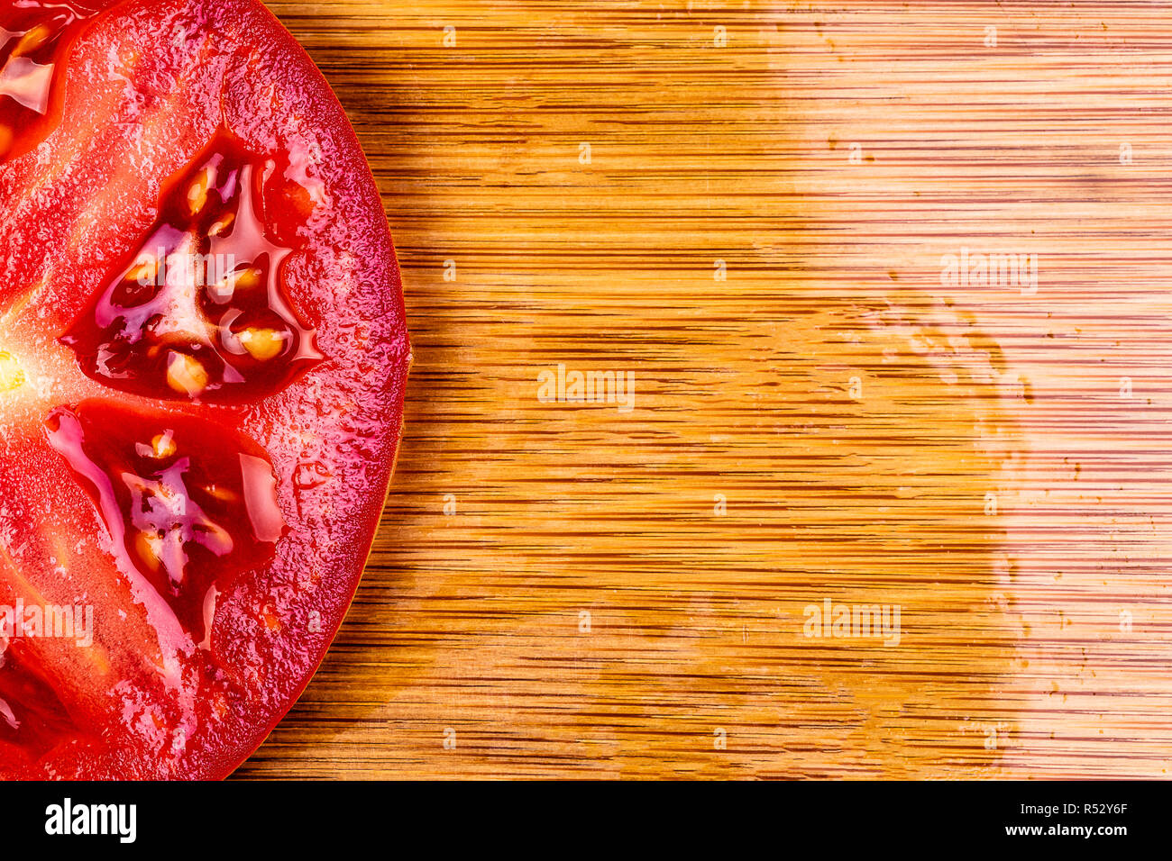 Ein Makro Abbild eines einzigen Tomate Scheibe auf einem Bambus Schneidebrett. Schuß zu liefern Kopie schriftlich Raum auf der rechten Seite der Scheibe. Schwerpunkt ist scharf und c Stockfoto