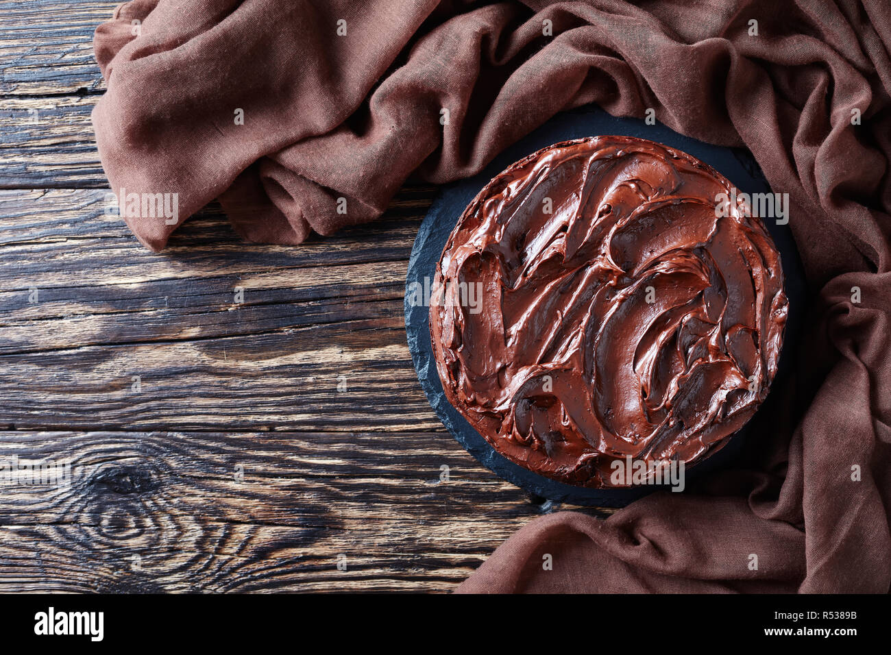 Schokoladentorte mit Marillenmarmelade und gekrönt mit Ganache auf einen schwarzen Stein Platte auf einem rustikalen Tabelle, Ansicht von oben, flach Stockfoto