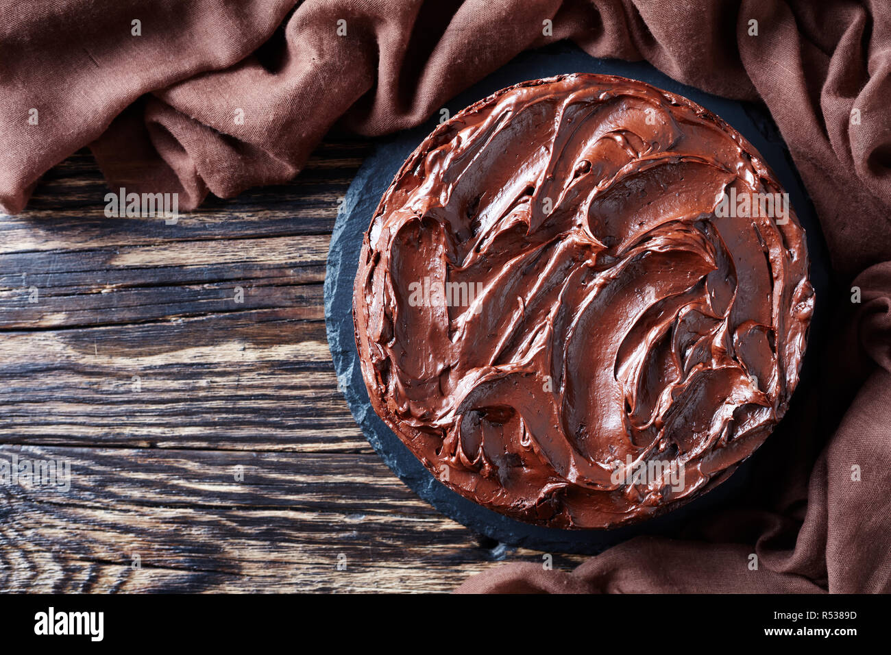 Hausgemachte Schokoladentorte mit Marillenmarmelade und gekrönt mit Ganache auf einem schwarzen Steinplatte mit braunen Tuch auf ein altes Holz- rustikalen Tab Stockfoto