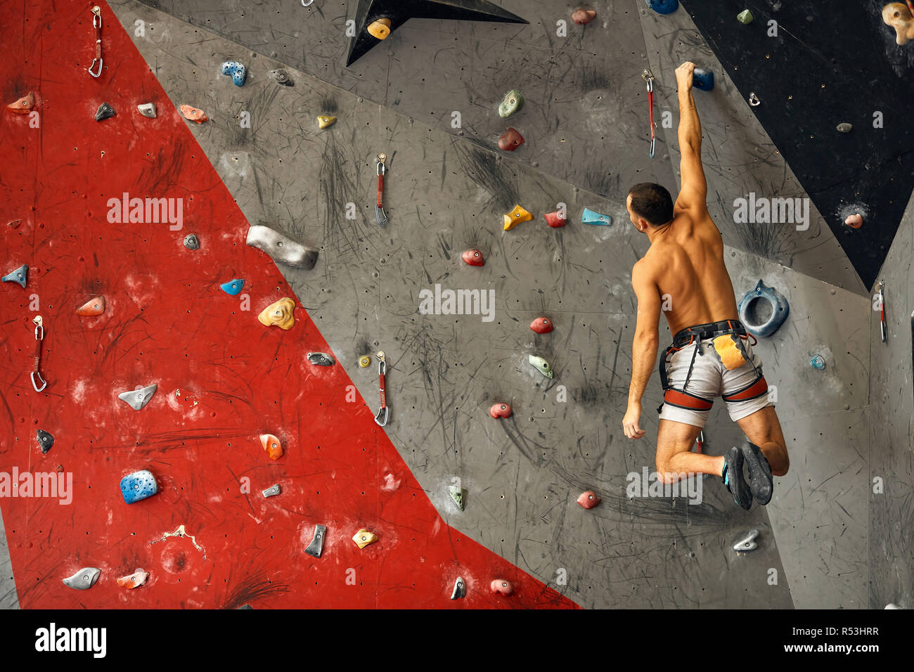 Junger Mann klettern in künstlichen Felsen, hängen an Sicherungsseilen Stockfoto