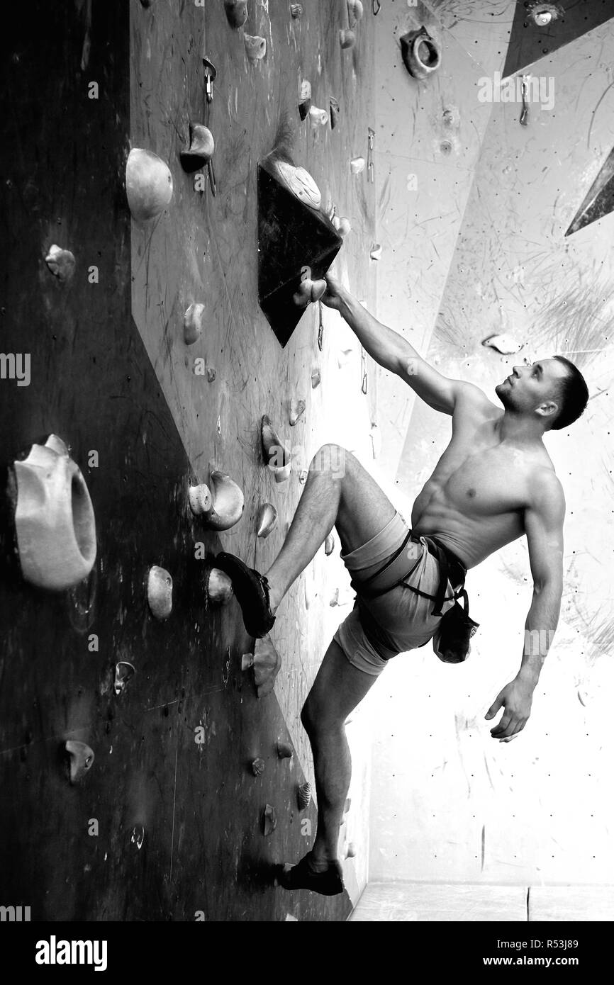 Männliche Kletterer das trainieren im Fitnessraum, Klettern bis auf künstliche Wand mit Felsbrocken. Stockfoto