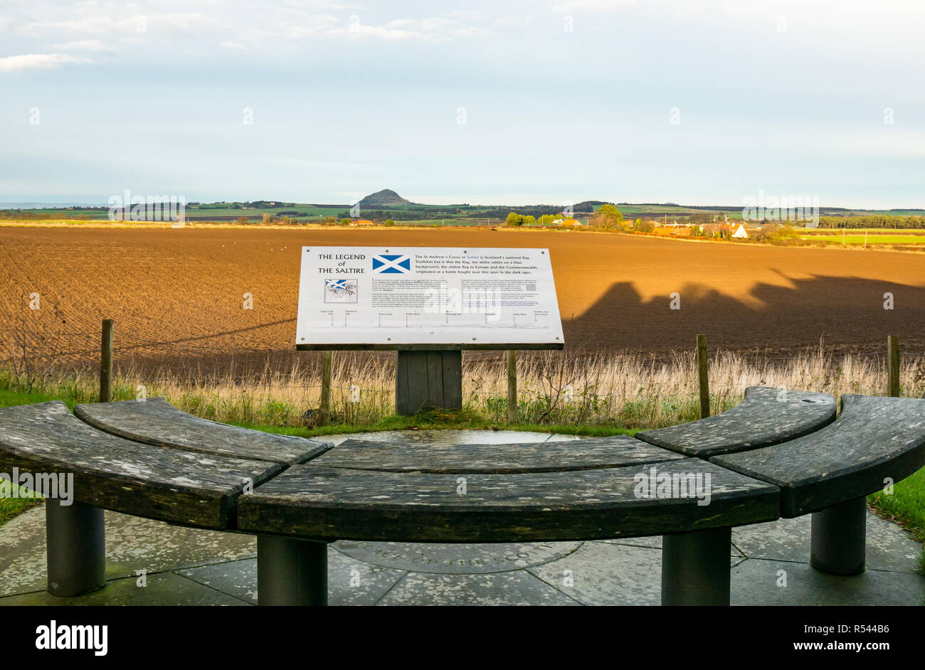 Athelstaneford, East Lothian, Schottland, Vereinigtes Königreich, 29. November 2018. Blick über die Felder bis Berwick Gesetz an der Geburtsstätte von St. Andrew's Cross, die saltire Flagge, mit einer Informationstafel und Sitzbank. Am Vorabend des St. Andrew's Day auf der nationalen Flagge Heritage Center. Die Legende sagt, dass am Vorabend der Schlacht zwischen Pikten und Winkel von Northumbria in 832 AD Saint Andrew hatte eine Vision von Sieg und wenn die Pikten sah ein weißes Kreuz durch Wolken im blauen Himmel sie ihren Sieg zu seinen Segen zugeschrieben, die Annahme des Kreuzes als Flag Stockfoto