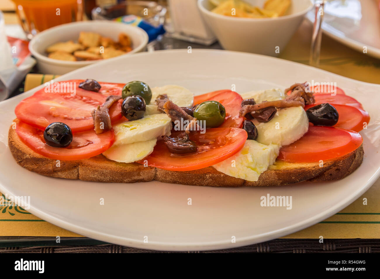 Mittagssnack von Tomaten, Käse. Sardellen und Oliven mit Brot, serviert auf einem weißen Teller. Stockfoto