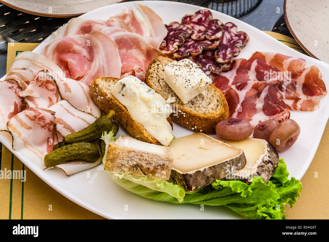 Auswahl an Aufschnitt und Käse mit Brot, Zwiebeln und Gurken, auf einem weißen Teller. Stockfoto