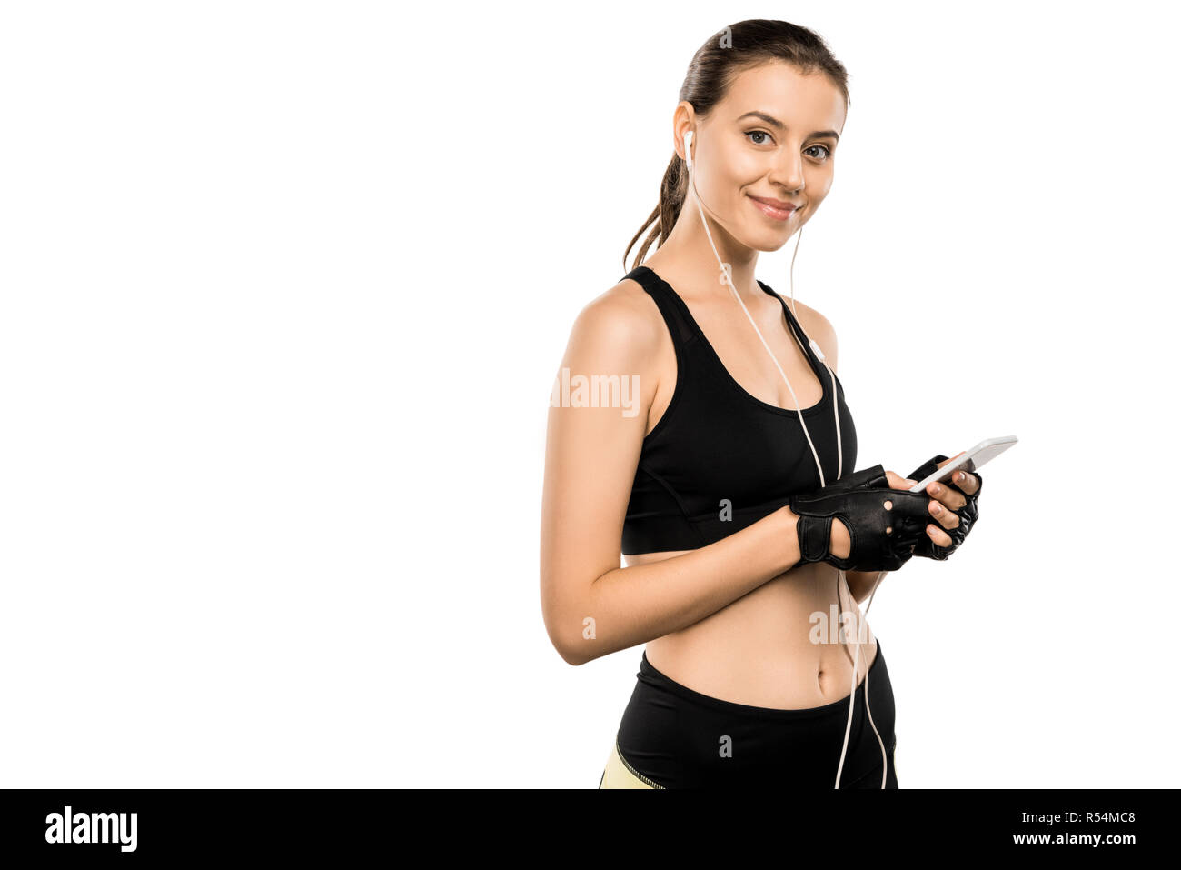 Attraktive Sportlerin im Gewichtheben Handschuhe und Ohrhörer mit Smartphone isoliert auf weißem Stockfoto