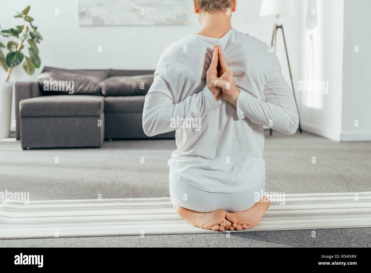 7/8 Schuß von Mann in Yoga sitting Pose mit Händen hinter Zurück zu Hause Stockfoto