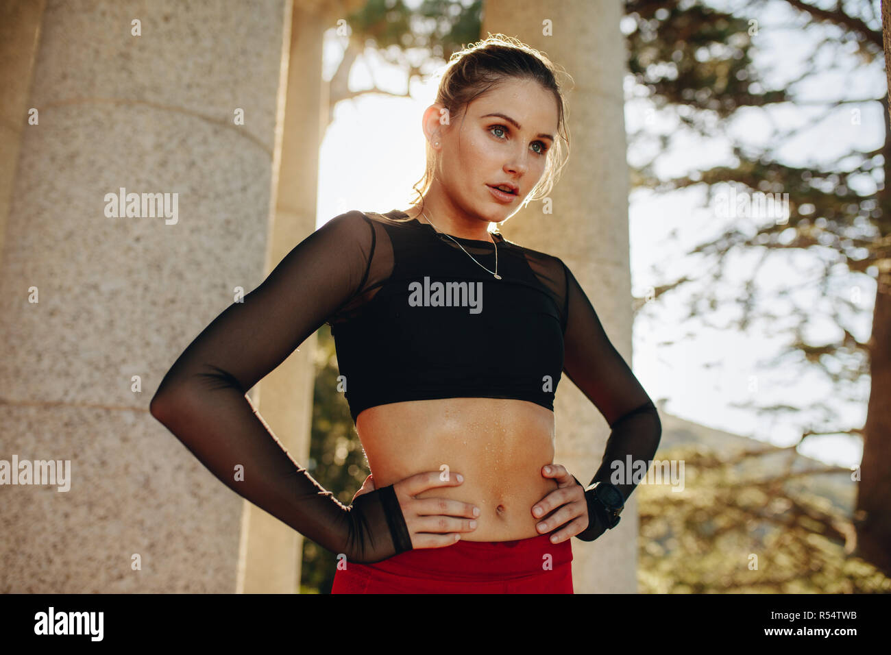 Fitness-Frau, die sich nach dem Workout mit Händen auf der Taille entspannt. Frau in Fitnesskleidung trainiert draußen mit Sonnenlicht im Hintergrund. Stockfoto