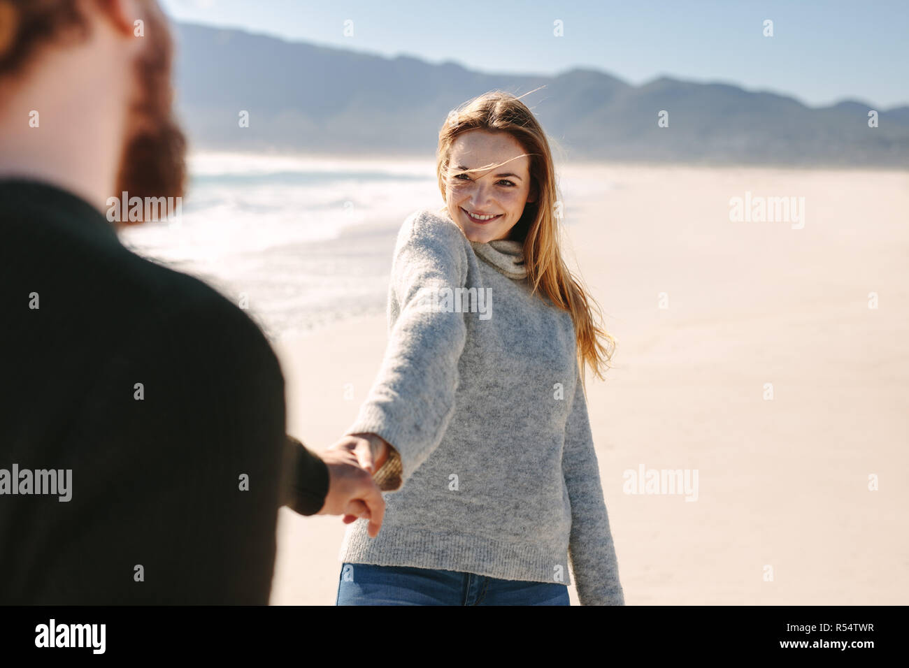 Lächelnd die hand Frau mit Mann bei einem Spaziergang am Strand. Glückliches junges Paar entlang der Se-Ufer. Stockfoto