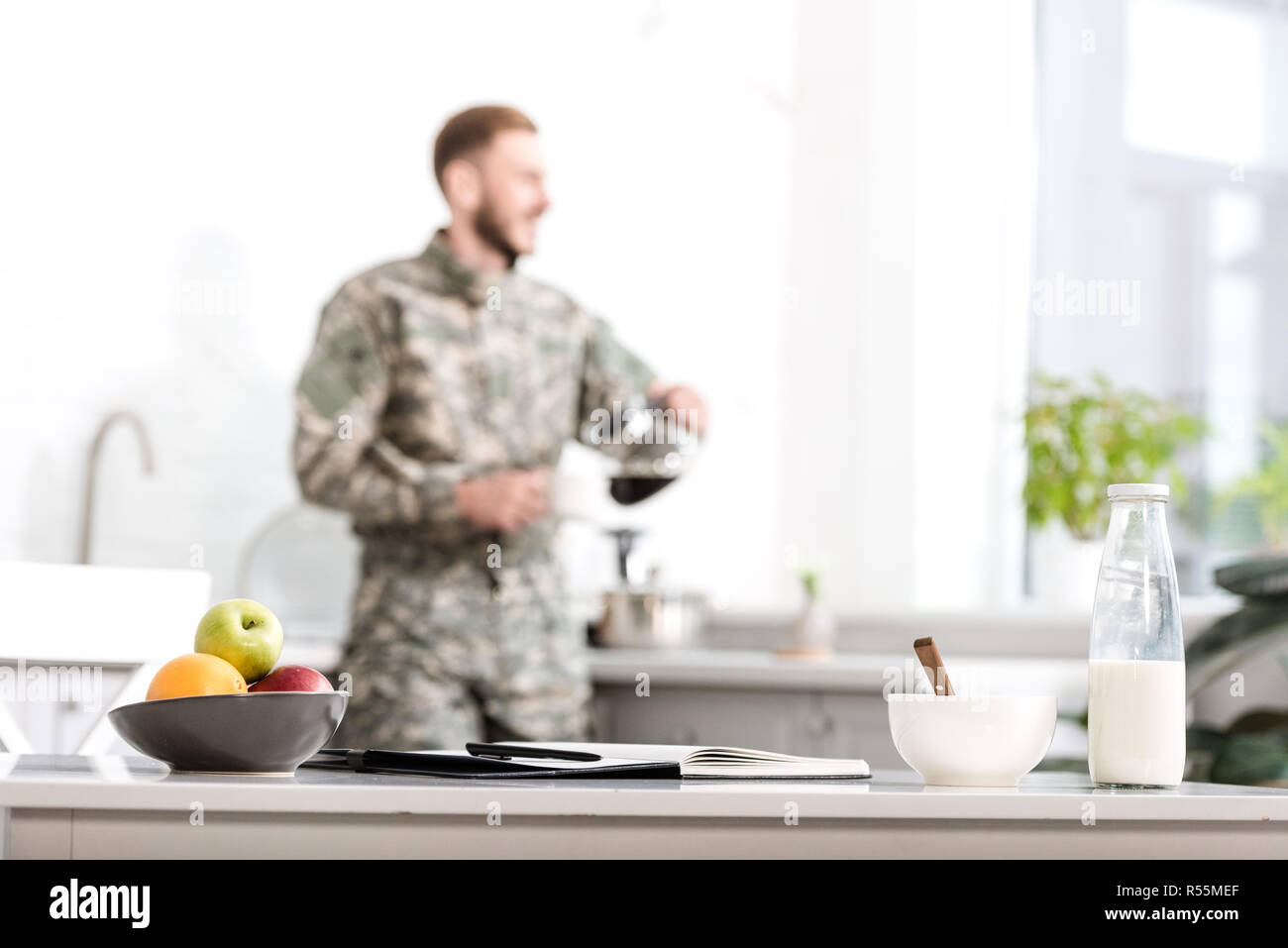 Selektiver Fokus der Tabelle mit Obst, Milch Flasche, Notizbuch und Stift, Armee, Soldat gießen gefilterten Kaffee in der Küche auf Hintergrund Stockfoto