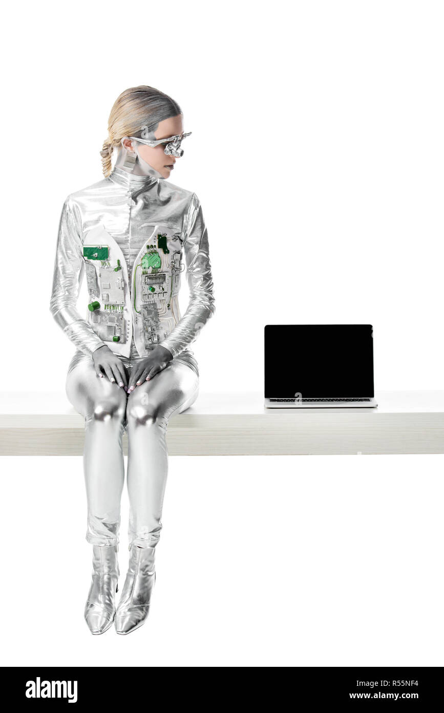 Silber Roboter sitzt am Tisch in der Nähe von Laptop mit leeren Bildschirm auf Weiß, zukünftige Technologie Konzept isoliert Stockfoto