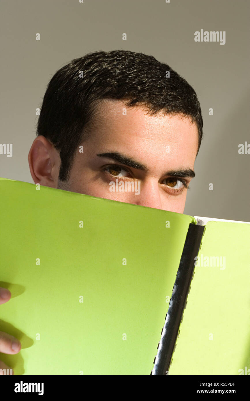 Männliche Schüler versteckt sich hinter einem Buch Stockfoto