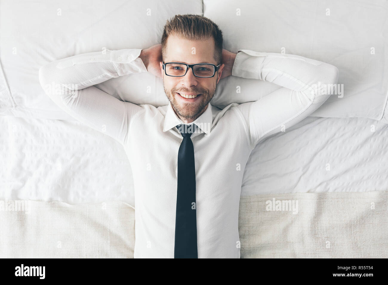 Ansicht von oben. Gut aussehender Geschäftsmann mit Brille liegend auf Bett Stockfoto